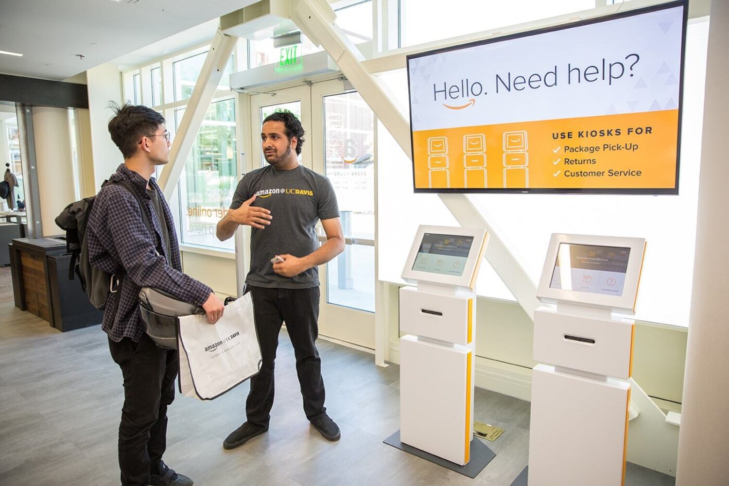 two men having a conversation in front of a amazon kiosk